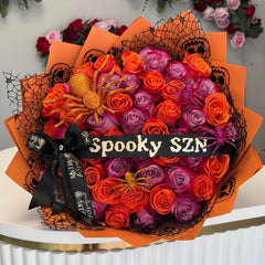 Halloween-themed bouquet with orange, purple, and pink roses on an orange paper background.